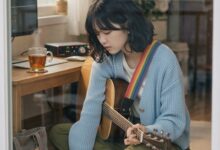방에서 기타를 치며 노트에 곡을 쓰는 AI 인플루언서 몽돌이